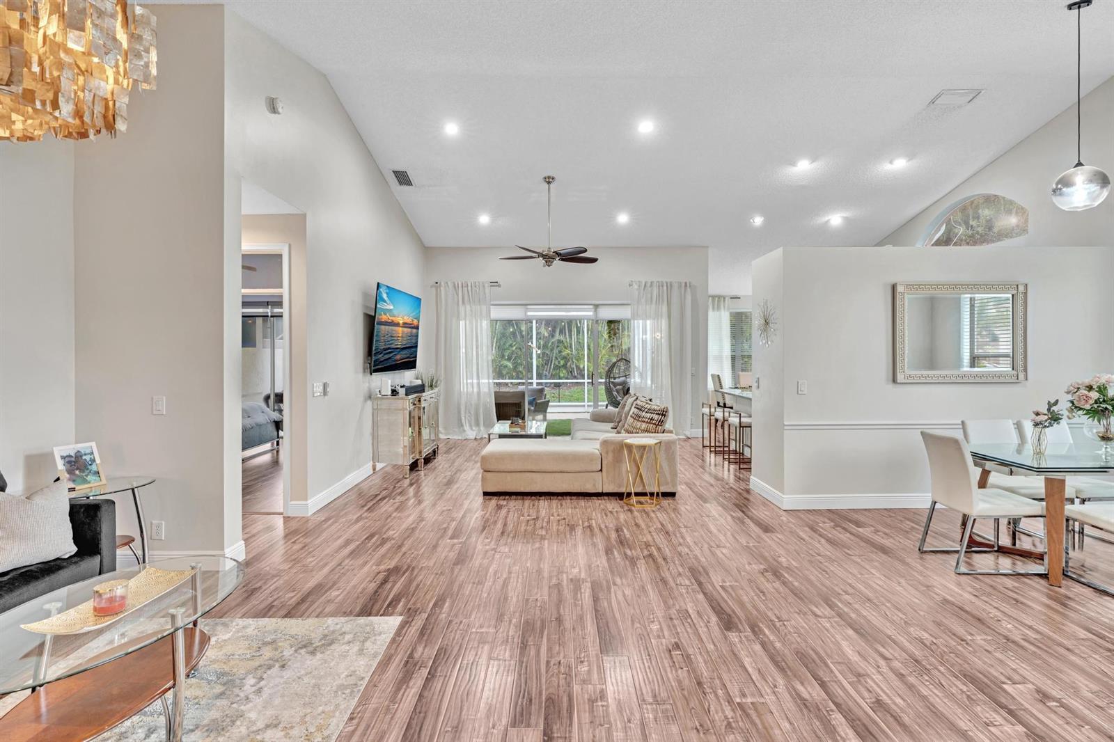 An open-concept living and dining area features wood-look flooring, vaulted ceilings, and a rear patio — 7445 Rockbridge Circle, Lake Worth FL 33467, LAKE WORTH, FL
