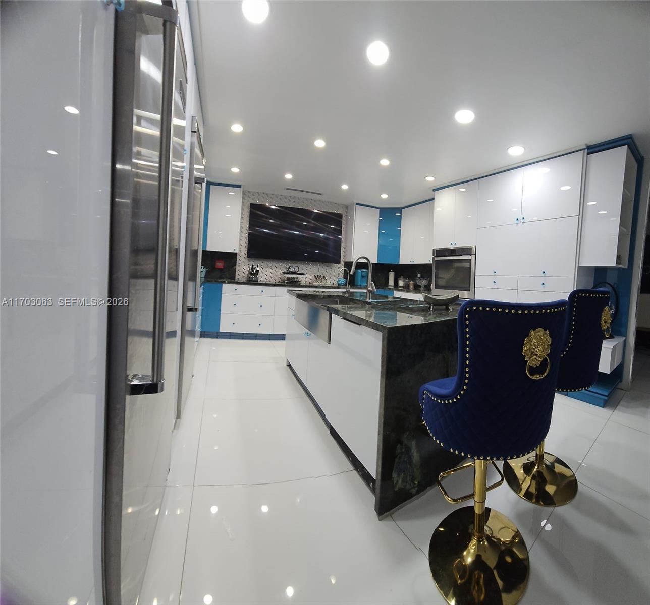 A modern kitchen features white cabinetry, blue accents, a dark stone island, and blue barstools — 15700 SW 202nd Ave, Miami FL 33187, MIAMI, FL
