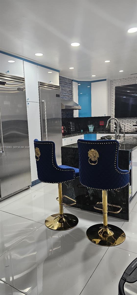 A modern kitchen features blue velvet bar stools with gold lion-head accents and stainless steel appliances — 15700 SW 202nd Ave, Miami FL 33187, MIAMI, FL