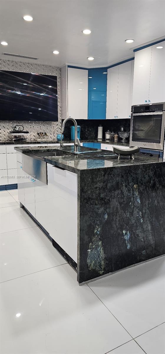 A modern kitchen features a large dark granite island, white cabinetry, and blue accents — 15700 SW 202nd Ave, Miami FL 33187, MIAMI, FL
