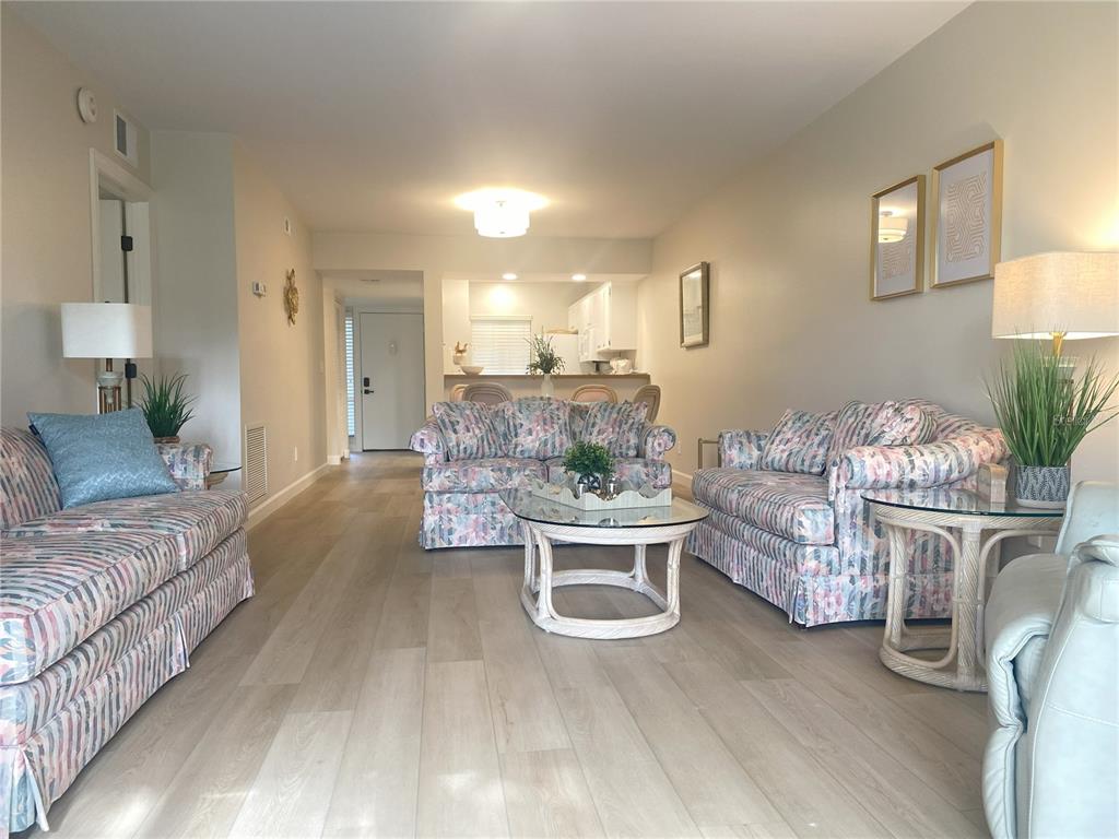 A living room features floral sofas, light wood-look flooring, and an open view to the kitchen — 796 BIRD BAY WAY UNIT Bld 30, VENICE, FL