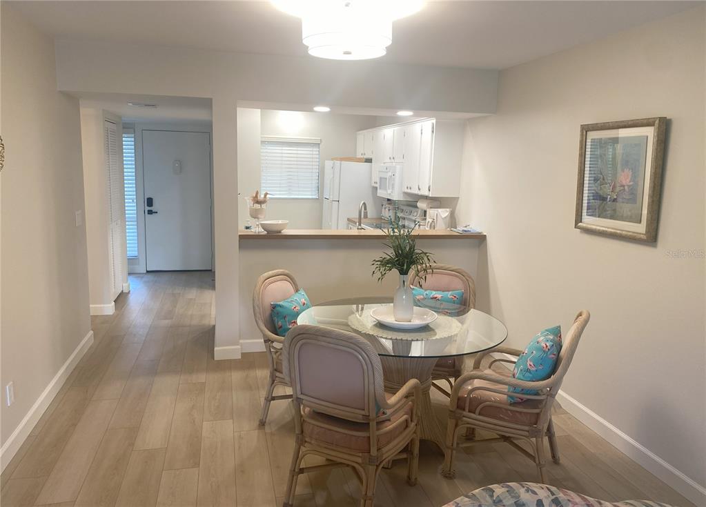 A dining area with a glass table and rattan chairs sits before an open kitchen — 796 BIRD BAY WAY UNIT Bld 30, VENICE, FL