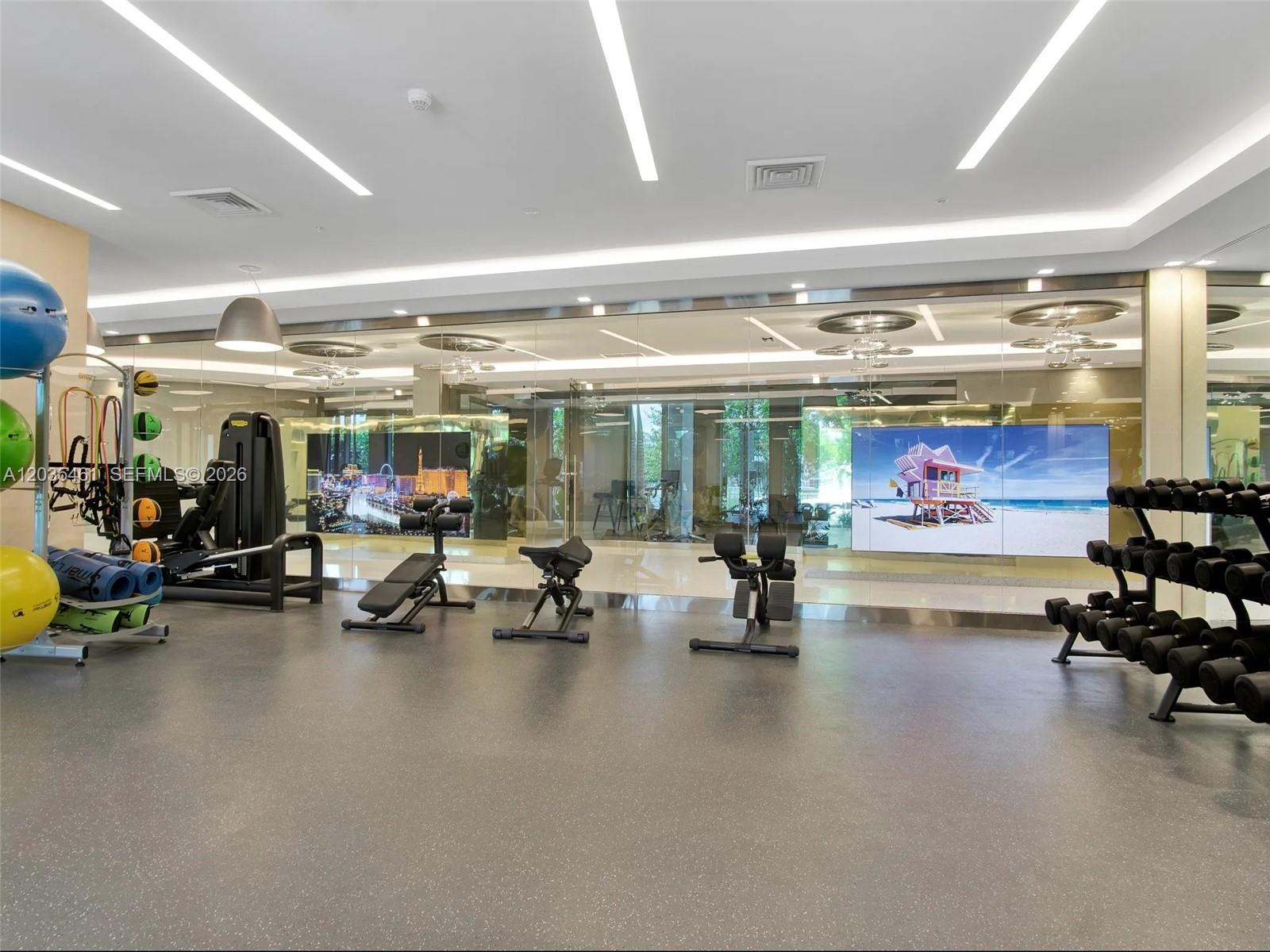 A modern gym features exercise equipment, mirrored walls, and large digital displays — 1000 NW 7th St # 310, Miami FL 33136, MIAMI, FL