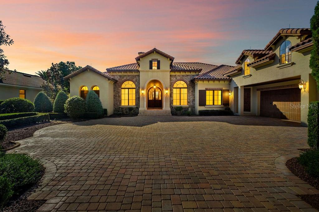 A Mediterranean-style house with a brick driveway and tall cypress trees at sunset — 6130 GROSVENOR SHORE DRIVE, WINDERMERE, FL