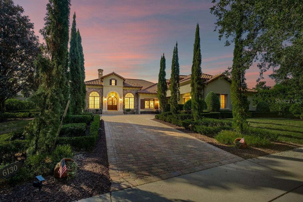 A large Mediterranean-style house features a stone facade, arched entryway, and a paved driveway — 6130 GROSVENOR SHORE DRIVE, WINDERMERE, FL