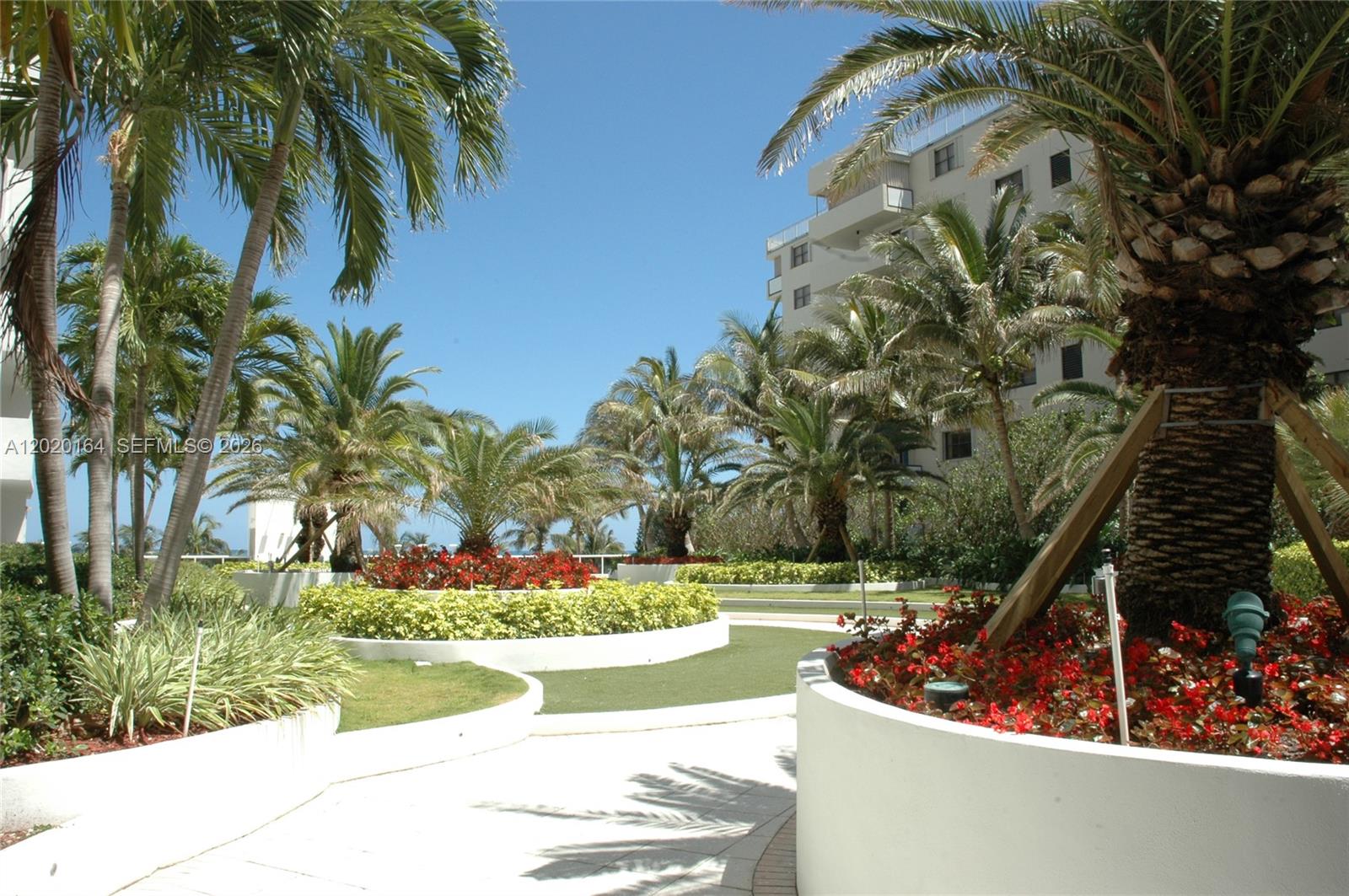 A sunny outdoor courtyard features palm trees, landscaped flower beds, and a paved walkway — 100 Lincoln Rd # 303, Miami Beach FL 33139, MIAMI BEACH, FL