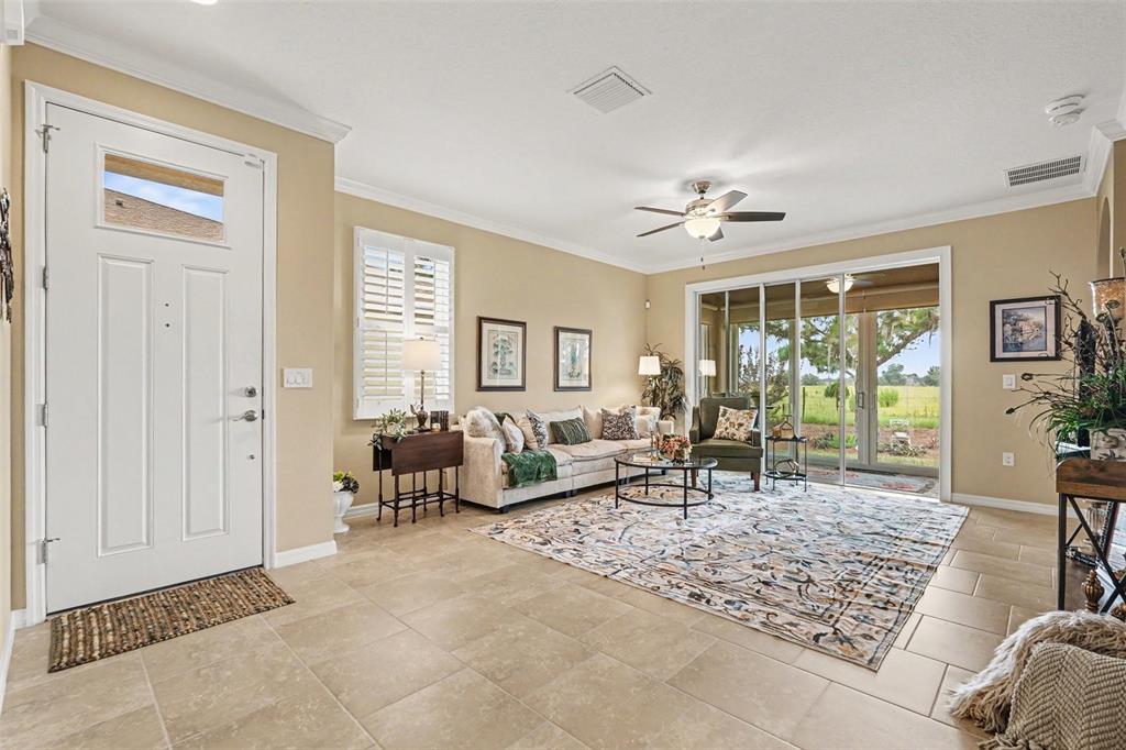 A living room with tile flooring, a beige sofa, a patterned rug, and sliding glass doors — 32983 WINDELSTRAW DRIVE, WESLEY CHAPEL, FL