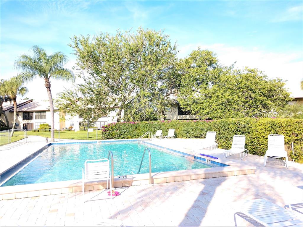 A rectangular swimming pool is surrounded by a paved deck, lounge chairs, and lush landscaping — 400 MISSION TRAIL E UNIT B, VENICE, FL