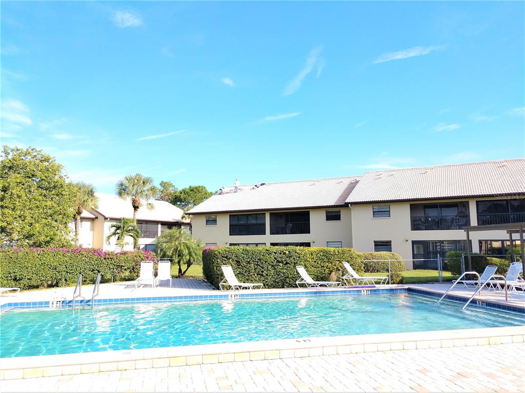 A swimming pool sits in front of a multi-story apartment building with a tiled roof — 400 MISSION TRAIL E UNIT B, VENICE, FL
