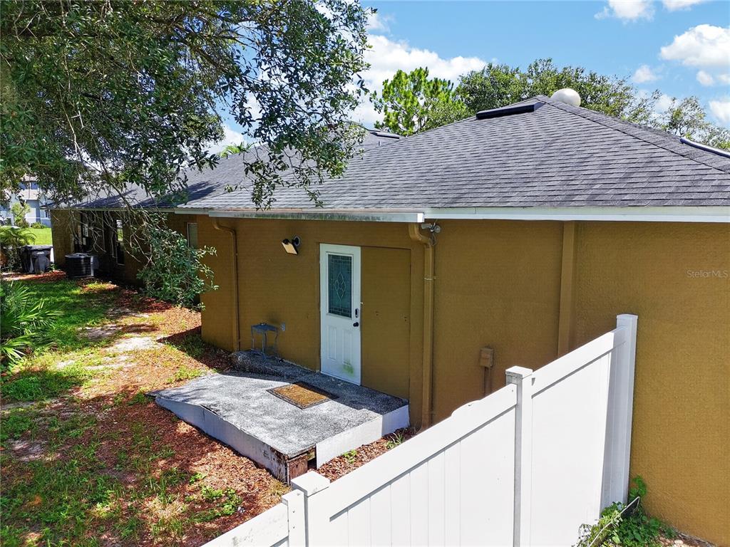 A side view of a house exterior featuring a white door, concrete stoop, and fence — 465 RIO GRANDE LANE, POINCIANA, FL
