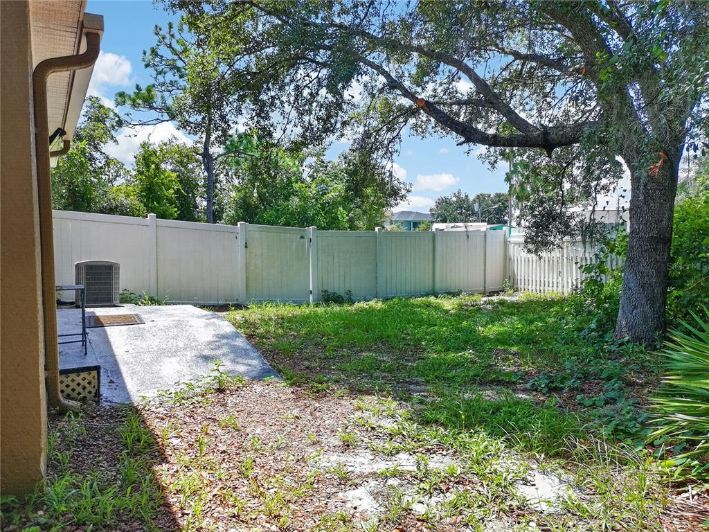 A backyard features a concrete patio, a white vinyl fence, and a large oak tree — 465 RIO GRANDE LANE, POINCIANA, FL