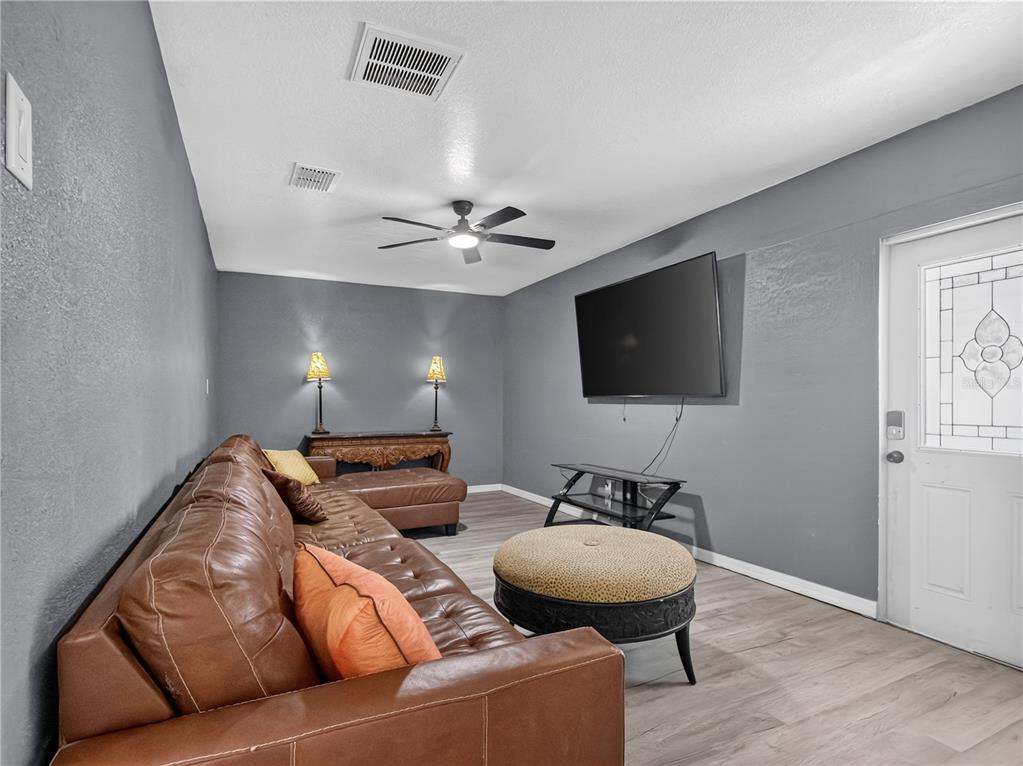 A living room features gray walls, wood-look flooring, a brown leather sectional, and a television — 465 RIO GRANDE LANE, POINCIANA, FL