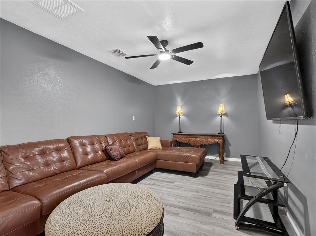 A living room features a brown leather sectional, a leopard-print ottoman, and gray flooring — 465 RIO GRANDE LANE, POINCIANA, FL
