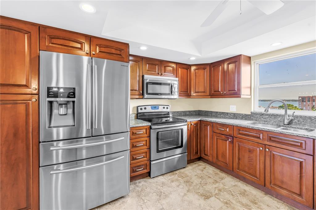 A kitchen with wood cabinets, stainless steel appliances, granite countertops, and a window overlooking water — 5108 BRITTANY DRIVE S UNIT 908, ST PETERSBURG, FL