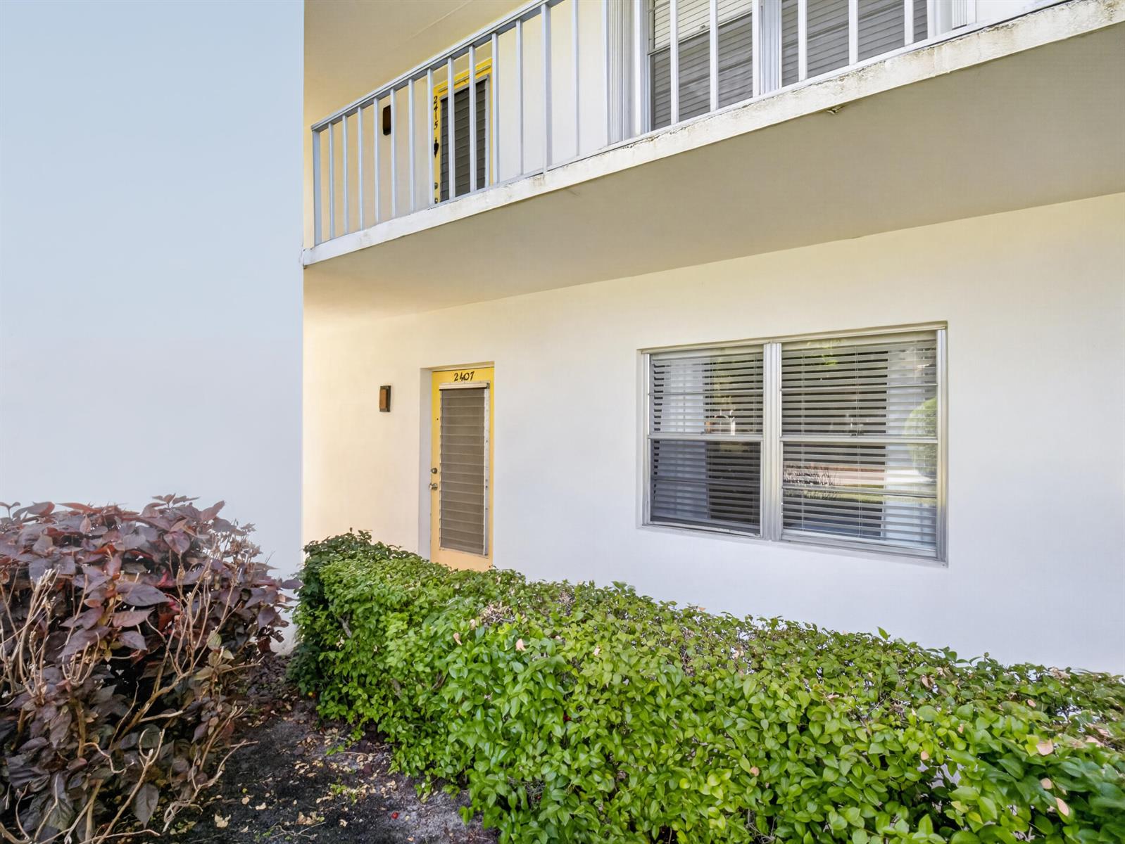 A two-story building exterior with a yellow door, a hedge, and a metal balcony railing — 1225 NW 21st Street # 2407, Stuart FL 34994, STUART, FL