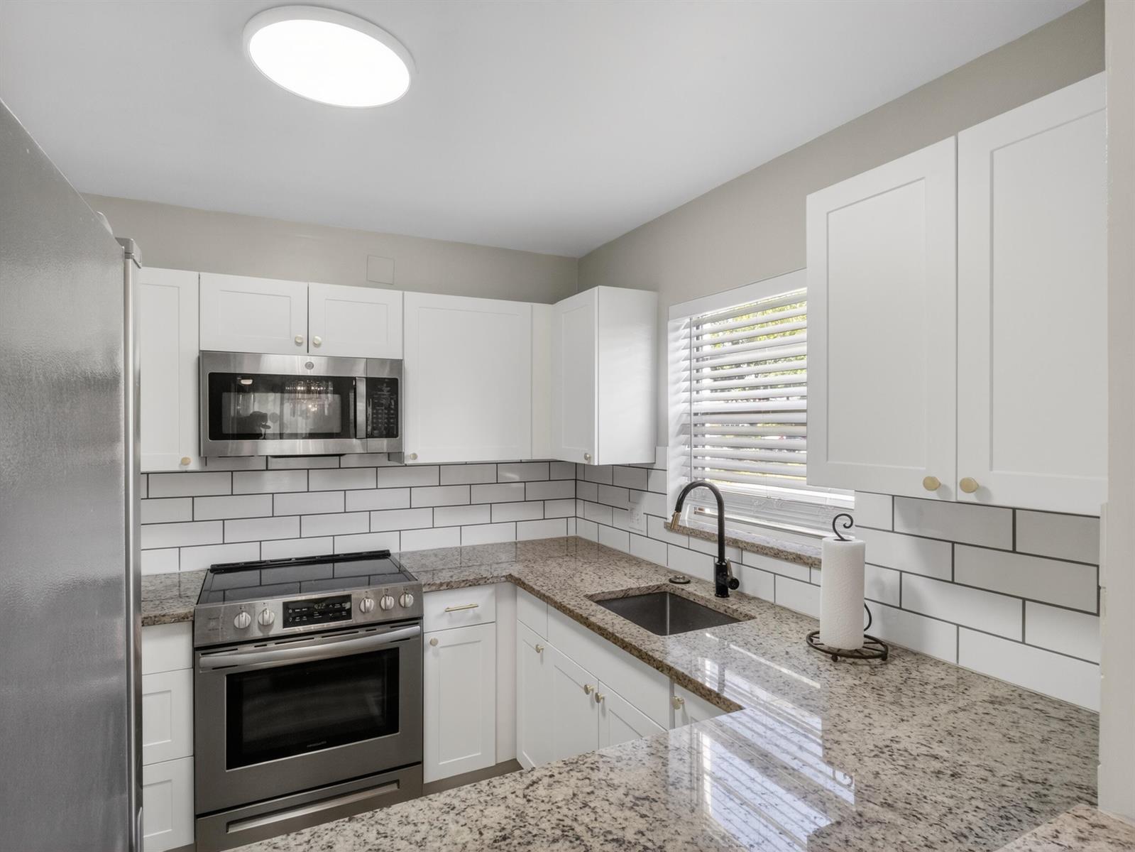 A kitchen features white cabinets, granite countertops, stainless steel appliances, and a subway tile backsplash — 1225 NW 21st Street # 2407, Stuart FL 34994, STUART, FL
