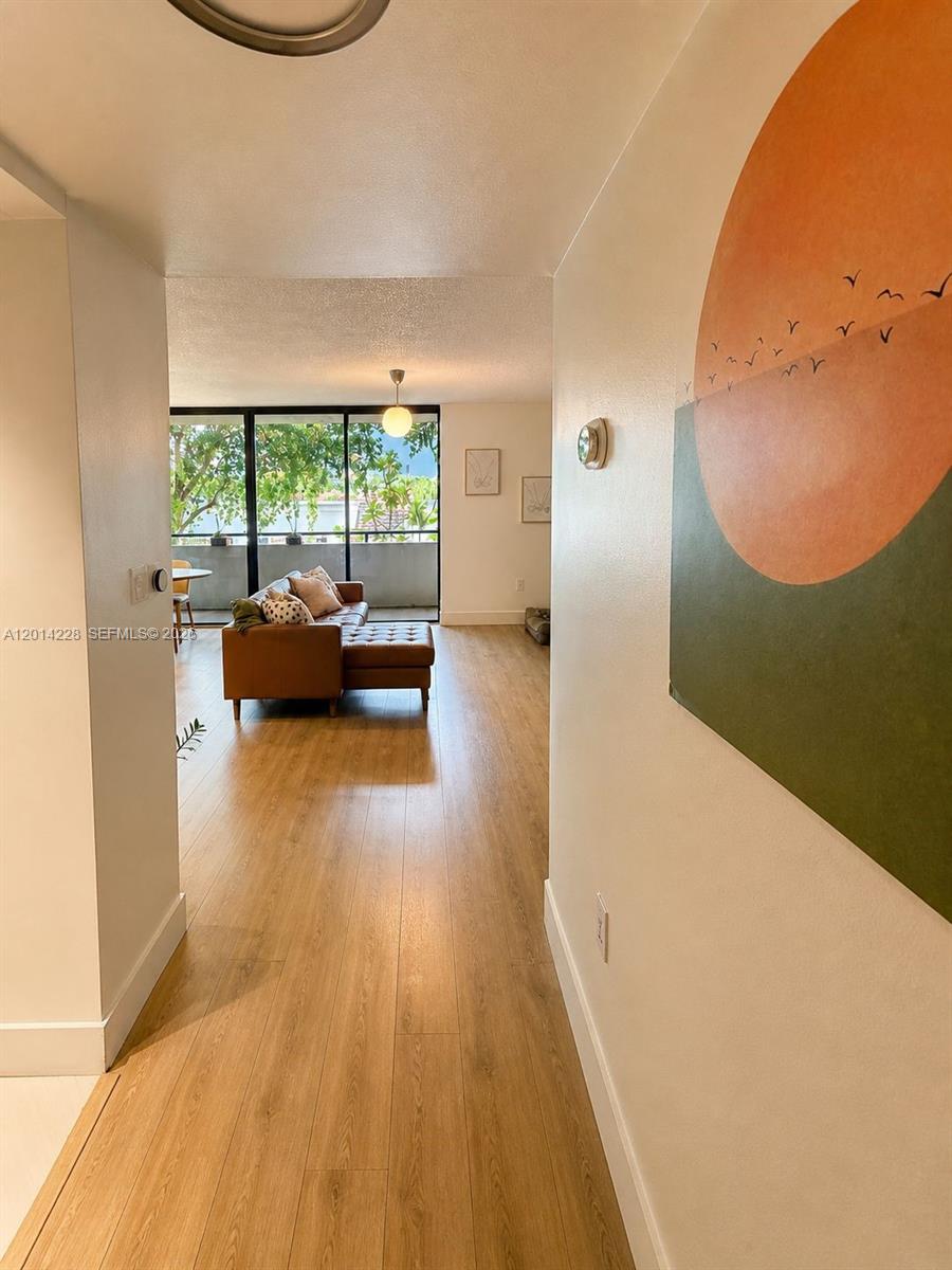 A hallway with light wood flooring leads to a living room with a balcony view — 21075 NE 34th Ave # 2, Aventura FL 33180, AVENTURA, FL
