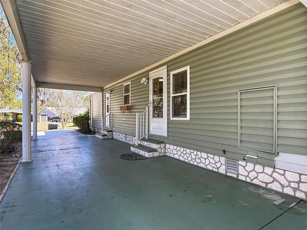 A covered concrete carport leads to the side entrance of a green-sided mobile home — 25533 BELLE HELENE, LEESBURG, FL