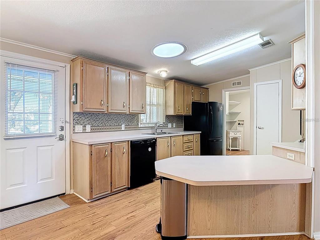 A kitchen features light wood cabinets, a black dishwasher, a black refrigerator, and laminate flooring — 25533 BELLE HELENE, LEESBURG, FL