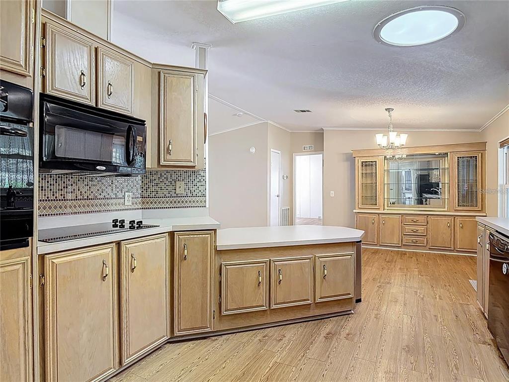 A kitchen with light wood cabinets, a mosaic backsplash, and an adjacent dining area — 25533 BELLE HELENE, LEESBURG, FL
