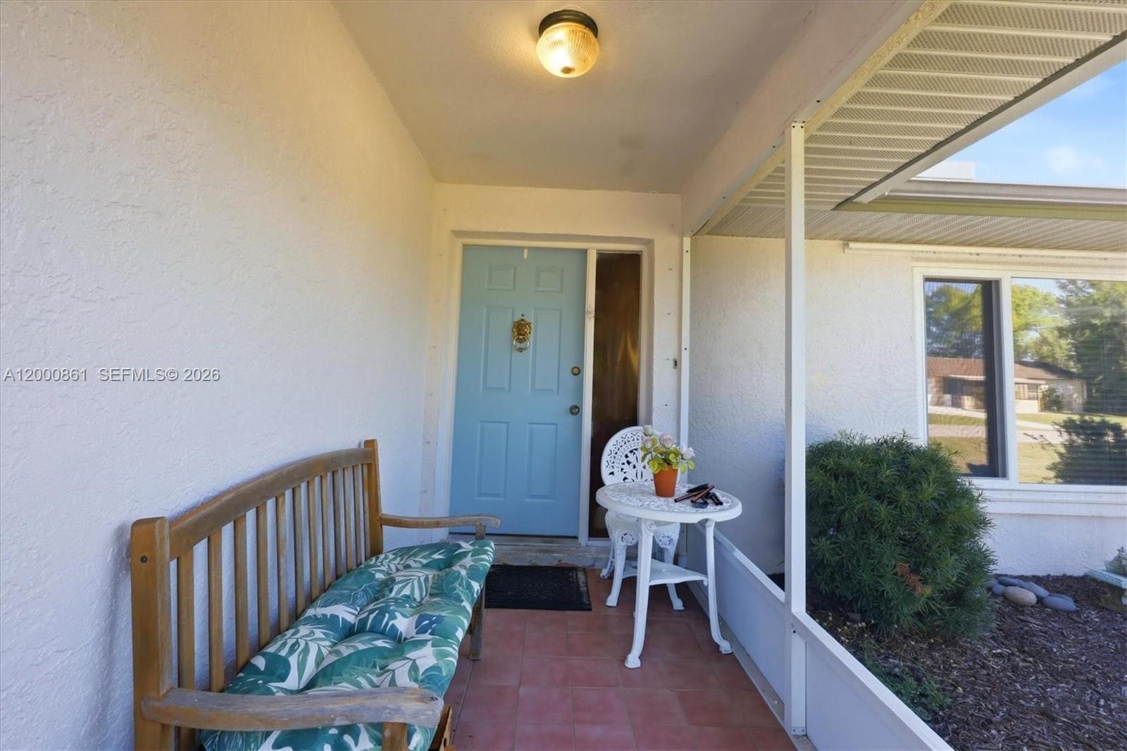 A covered front porch features a wooden bench, a small bistro set, and a blue door — PORT CHARLOTTE, FL