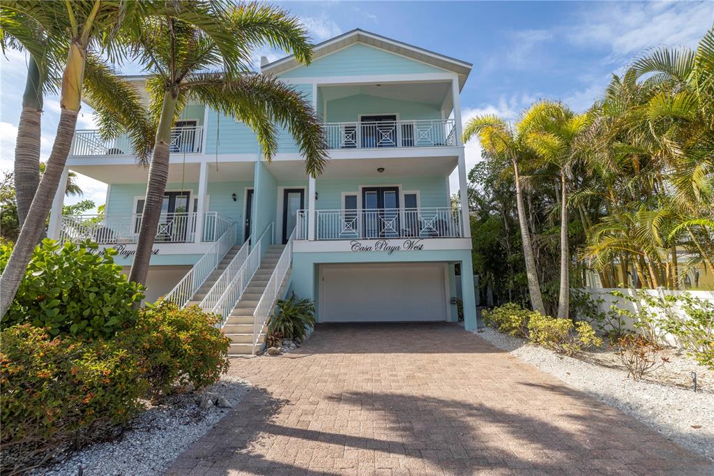 A light blue two-story house with a paved driveway, palm trees, and elevated balconies — 105 4TH STREET S, BRADENTON BEACH, FL