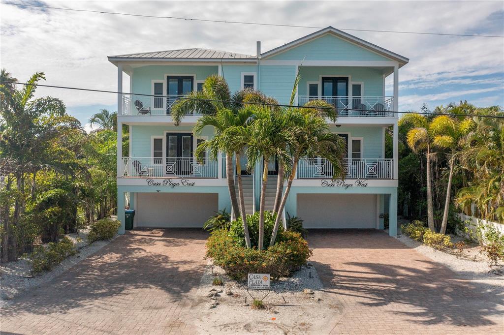 A two-story light blue beach house with two garage bays and palm trees in front — 105 4TH STREET S, BRADENTON BEACH, FL