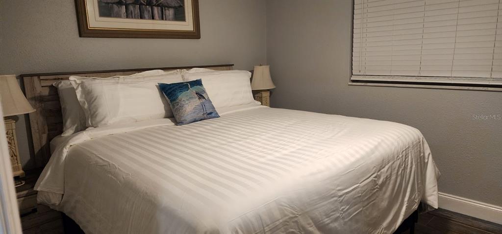 A bedroom features a king-sized bed with white striped bedding and a decorative accent pillow — 5053 N BEACH ROAD UNIT 9E/W, ENGLEWOOD, FL