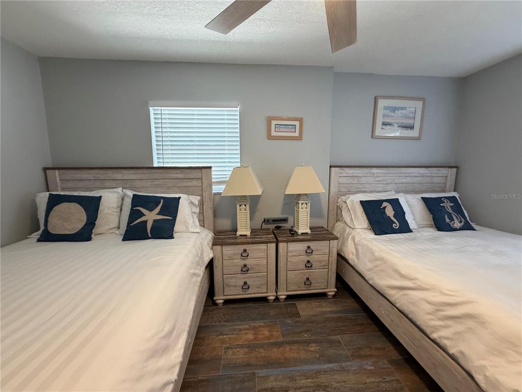 A bedroom features two beds with nautical pillows, two nightstands, and wood-look tile flooring — 5053 N BEACH ROAD UNIT 9E/W, ENGLEWOOD, FL