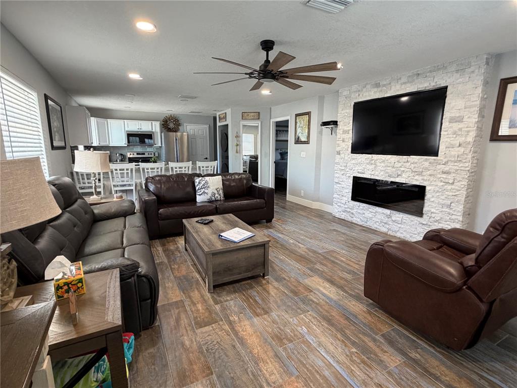 A living room with wood-look tile floors, a stone fireplace, and an open kitchen — 5053 N BEACH ROAD UNIT 9E/W, ENGLEWOOD, FL