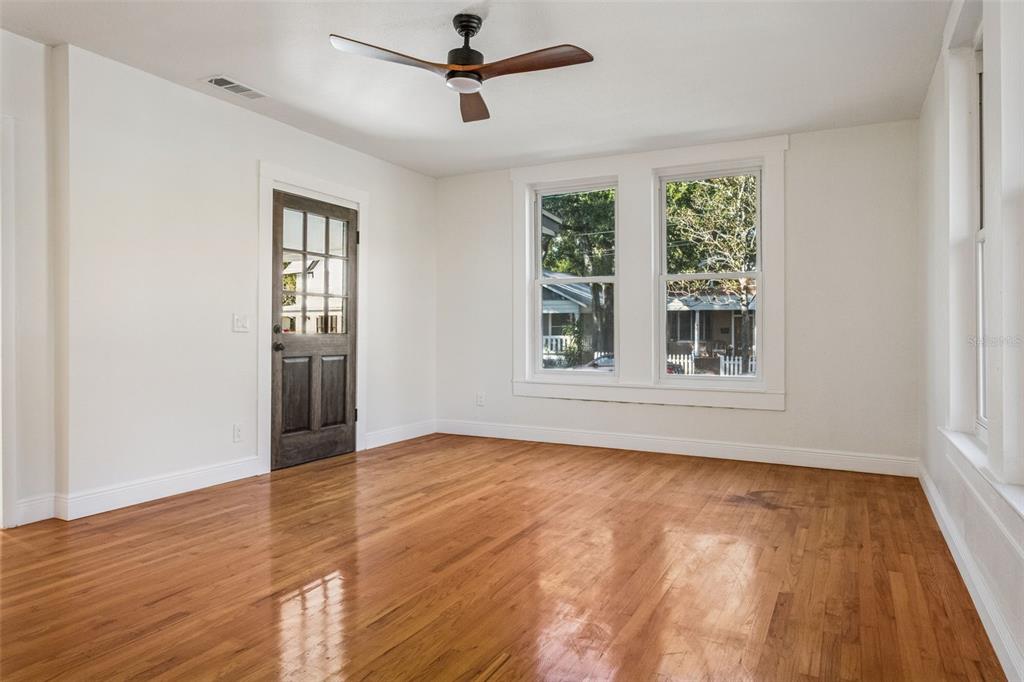 An empty room with hardwood floors, a ceiling fan, a dark door, and two windows — 511 E FRANCES AVENUE, TAMPA, FL
