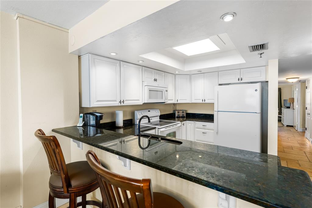 A kitchen features white cabinets, dark granite countertops, a breakfast bar, and white appliances — 4139 S. ATLANTIC AVENUE UNIT B504, NEW SMYRNA BEACH, FL