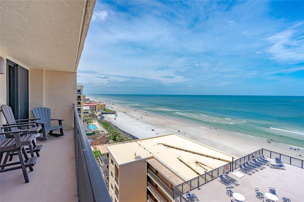 A balcony with chairs overlooks a sandy beach and the ocean from a high-rise building — 4139 S. ATLANTIC AVENUE UNIT B504, NEW SMYRNA BEACH, FL
