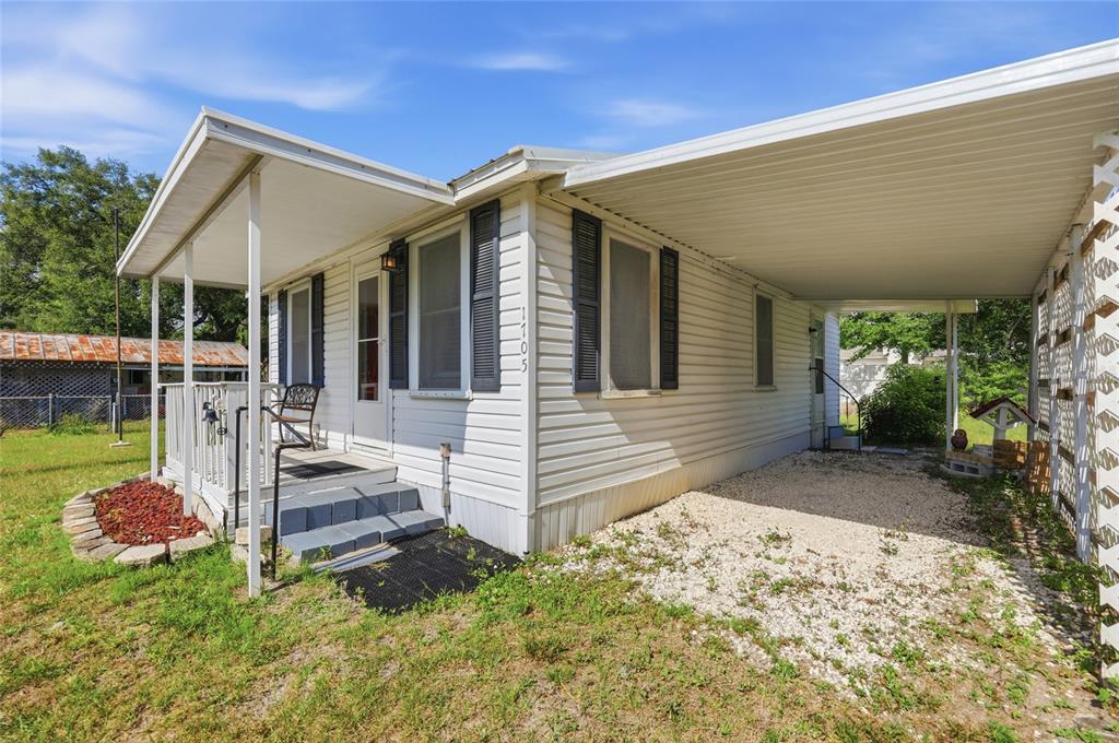 A white mobile home with a covered porch, carport, and gravel driveway under a blue sky — 1705 DELAWARE AVENUE, ST CLOUD, FL