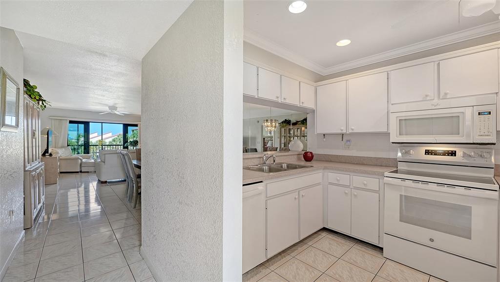 A white kitchen with a pass-through window overlooks a living area with tile flooring — 6234 MIDNIGHT PASS ROAD UNIT 307, SARASOTA, FL