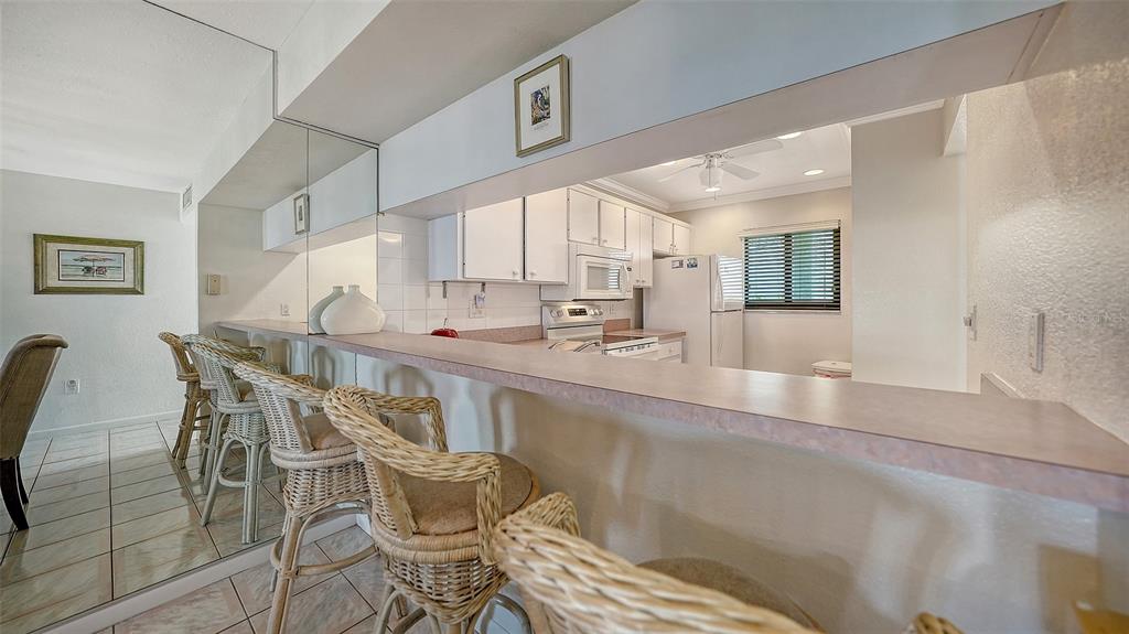 A kitchen with white cabinets and a breakfast bar featuring wicker stools and mirrored walls — 6234 MIDNIGHT PASS ROAD UNIT 307, SARASOTA, FL