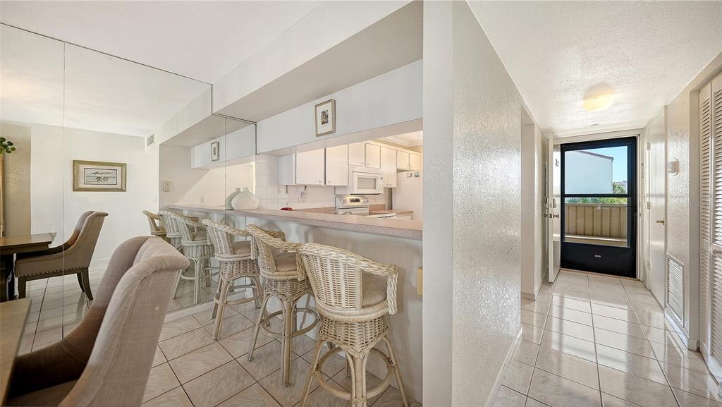 A kitchen with a breakfast bar and wicker stools opens to a tiled dining area — 6234 MIDNIGHT PASS ROAD UNIT 307, SARASOTA, FL
