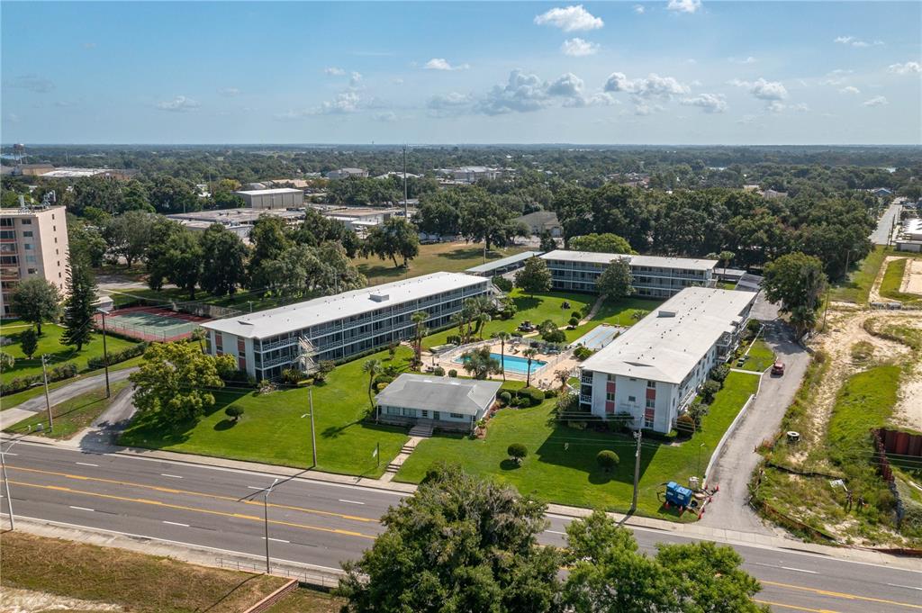 An aerial view shows three apartment buildings, a swimming pool, and a tennis court — 1700 6TH STREET NW UNIT C26, WINTER HAVEN, FL
