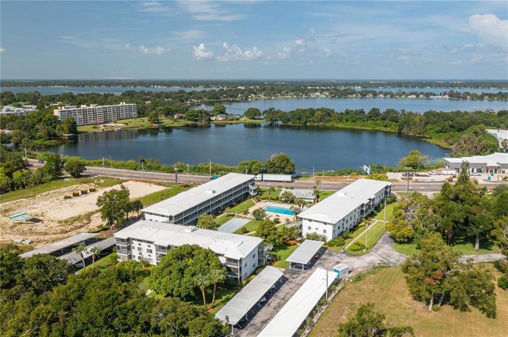 An aerial view shows apartment buildings with a swimming pool near a large lake — 1700 6TH STREET NW UNIT C26, WINTER HAVEN, FL