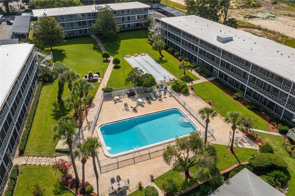 An aerial view shows a swimming pool, shuffleboard courts, and apartment buildings with green lawns — 1700 6TH STREET NW UNIT C26, WINTER HAVEN, FL