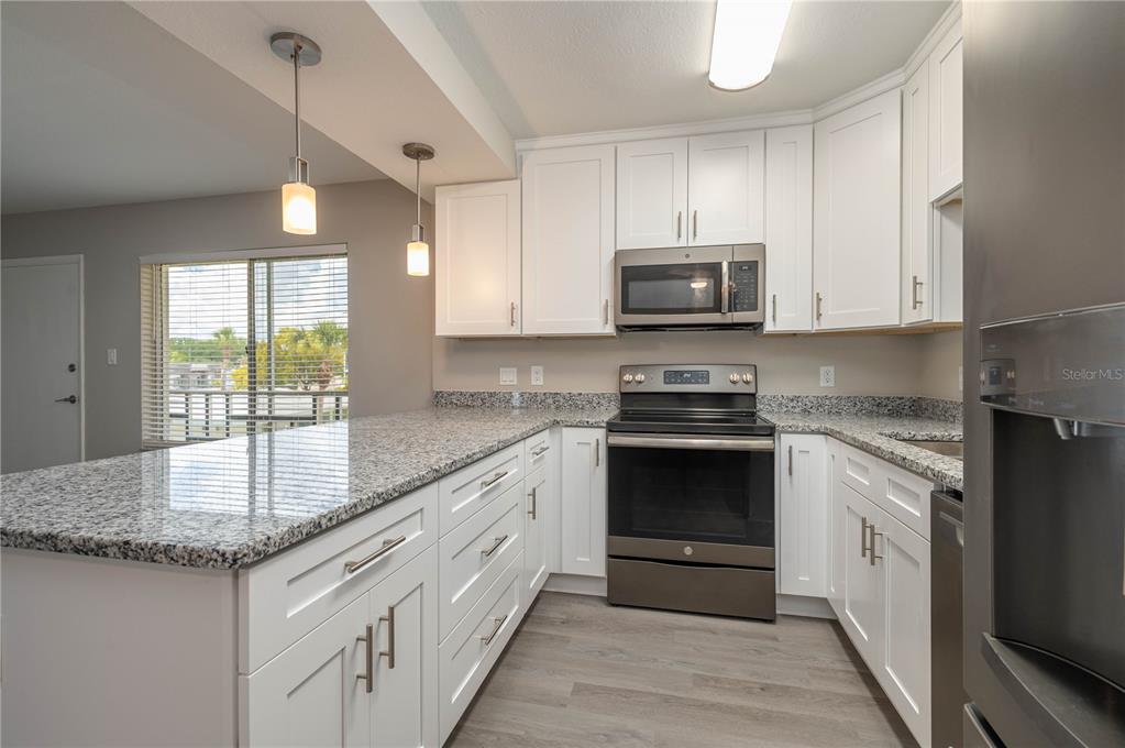 A kitchen with white cabinets, granite countertops, stainless steel appliances, and light wood-look flooring — 1700 6TH STREET NW UNIT C26, WINTER HAVEN, FL