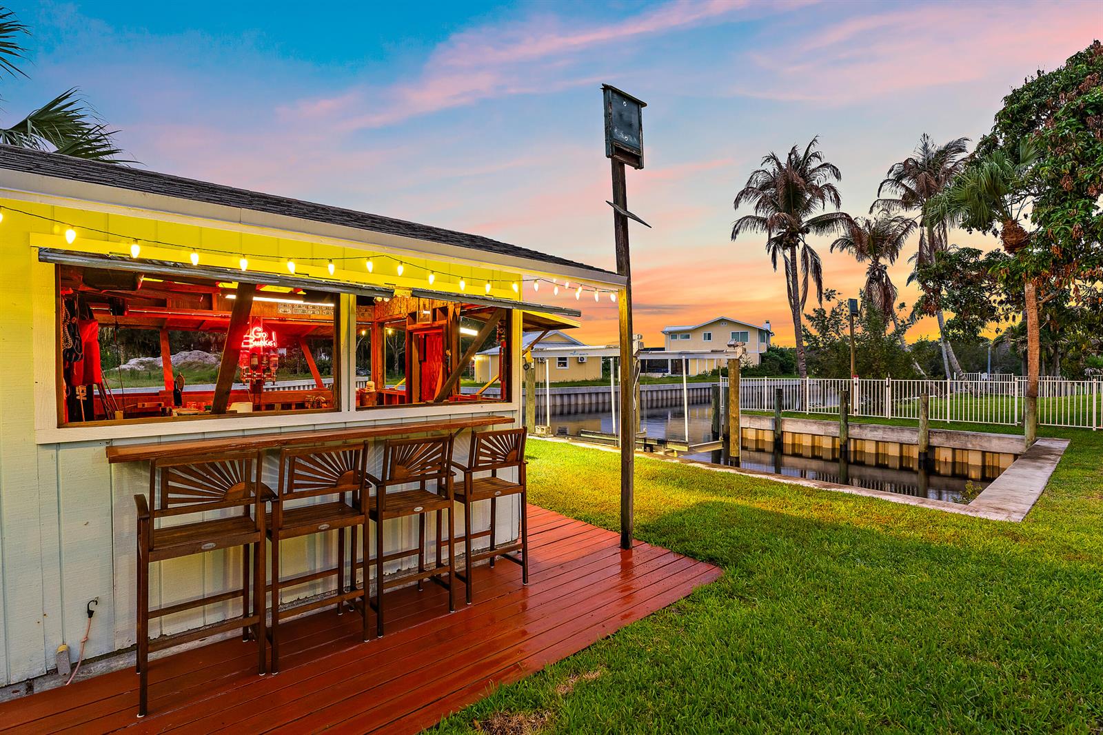 An outdoor tiki bar with wooden stools sits on a deck beside a canal — 715 SW Rustic Circle, Stuart FL 34997, STUART, FL