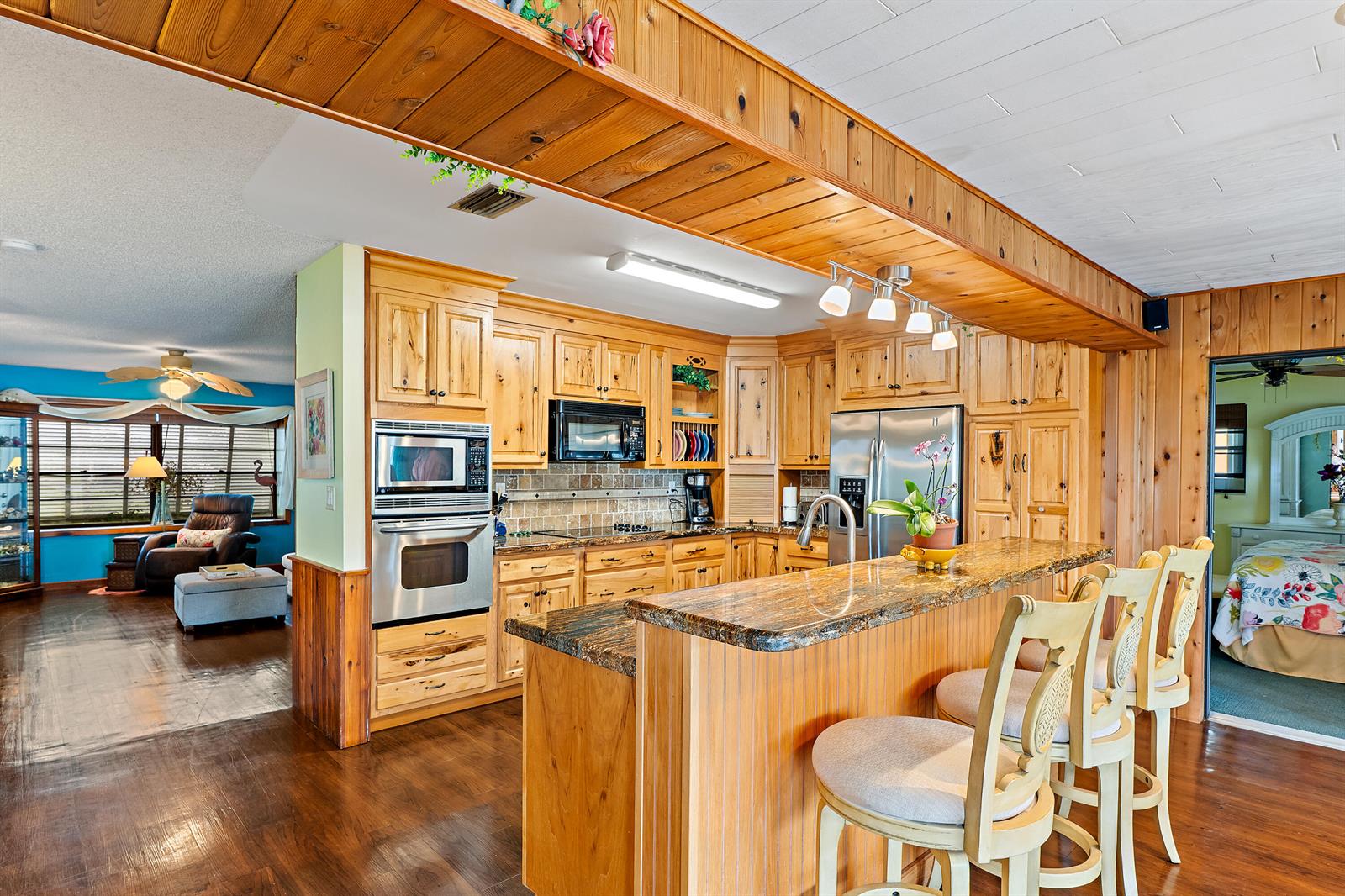 A kitchen with wood cabinets, granite countertops, and a breakfast bar overlooks a living area — 715 SW Rustic Circle, Stuart FL 34997, STUART, FL