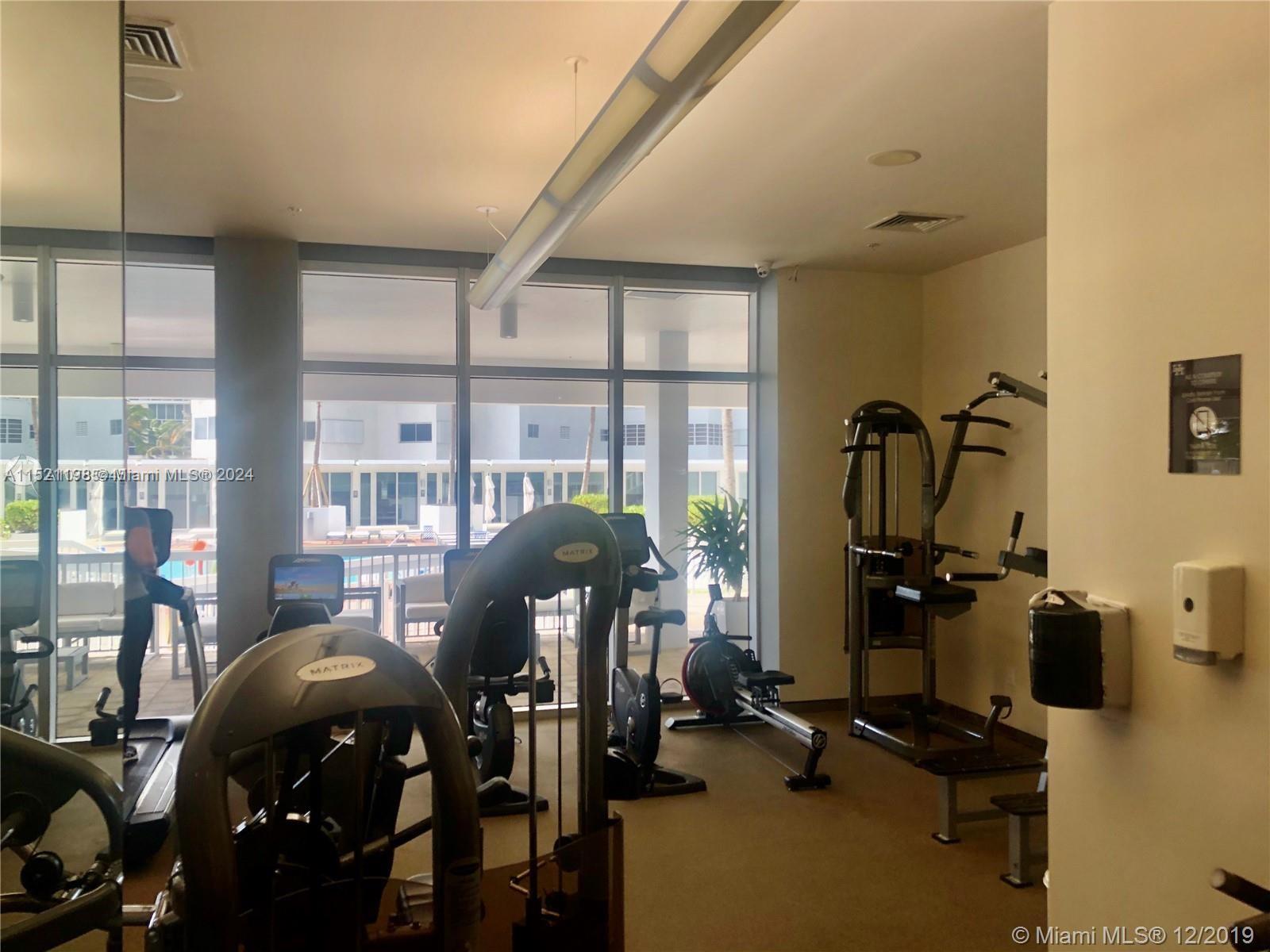 This fitness center features various exercise machines, floor-to-ceiling windows, and a view of a pool — 10275 Collins Ave # 230, Bal Harbour FL 33154, BAL HARBOUR, FL
