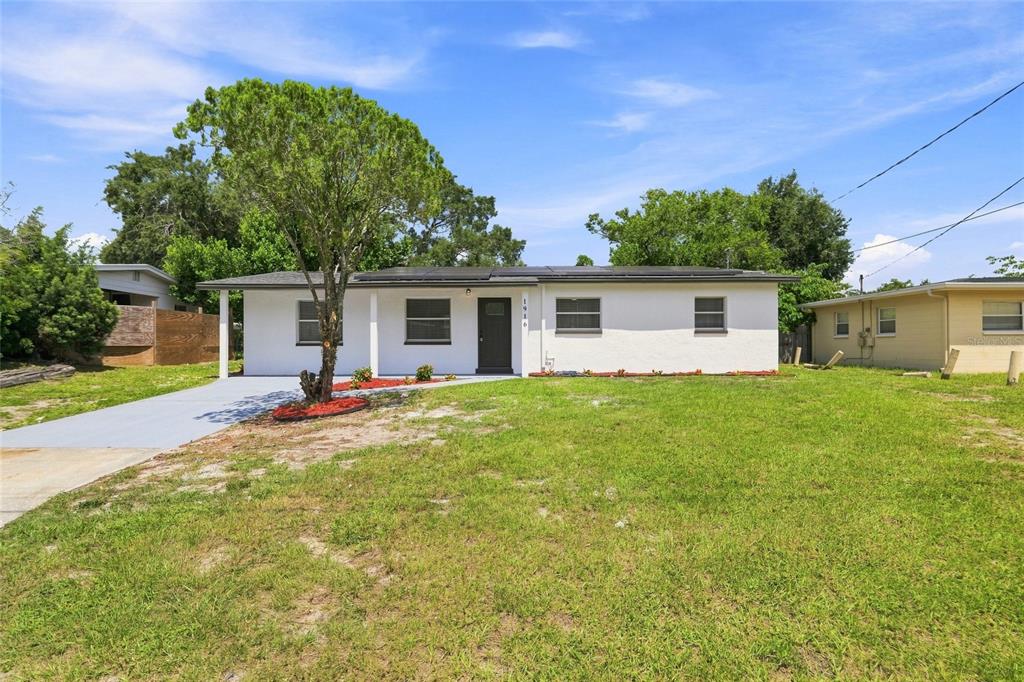 A single-story white house with a dark front door and solar panels on the roof — 1916 MARVY AVENUE, TAMPA, FL