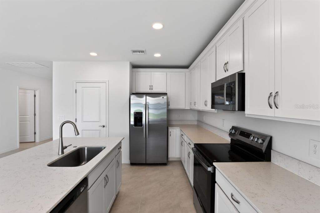 A kitchen with white cabinets, stainless steel appliances, and a quartz-topped island with a sink — 9509 VIBRANT LANE, VENICE, FL