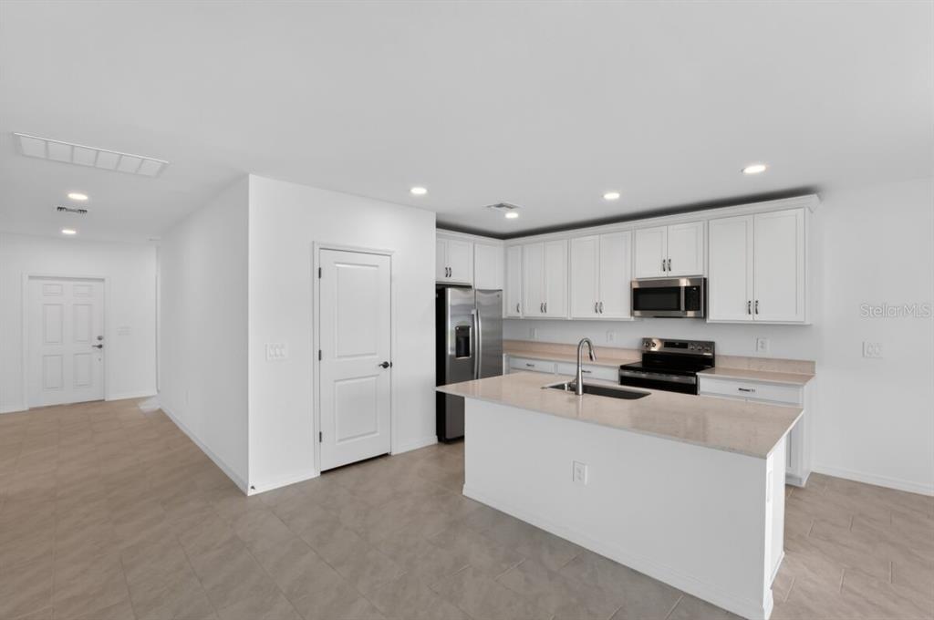 A modern kitchen features white cabinets, stainless steel appliances, a center island, and tile flooring — 9509 VIBRANT LANE, VENICE, FL