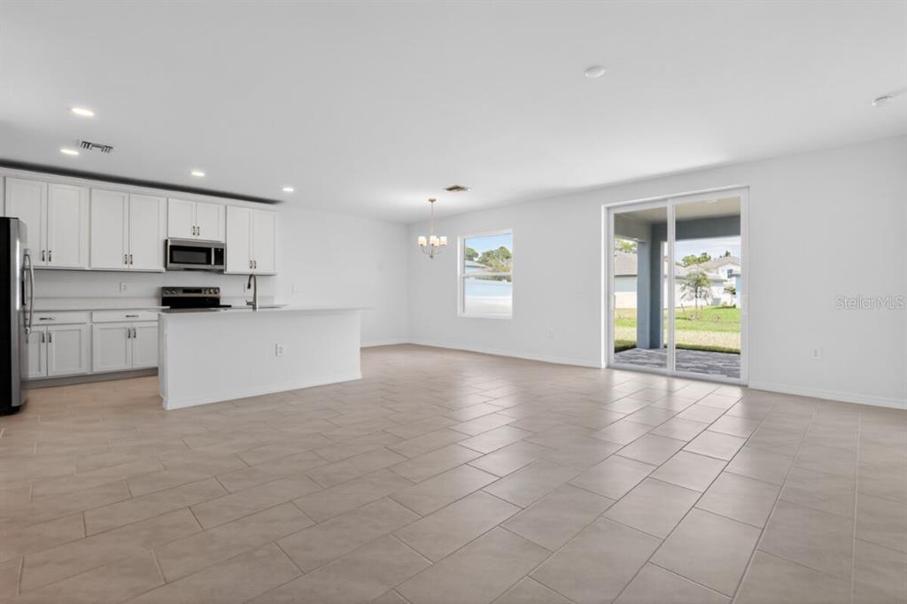 A kitchen with white cabinets and an island opens to a tiled dining and living area — 9509 VIBRANT LANE, VENICE, FL