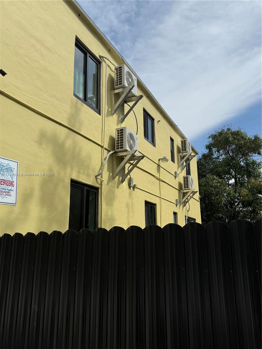 The exterior of a yellow building features multiple wall-mounted air conditioning units and black windows — 5501 NW Miami Ct, Miami FL 33127, MIAMI, FL