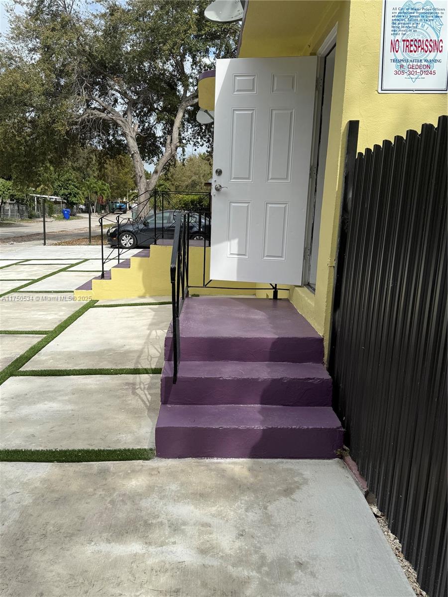 A white door opens onto purple concrete steps leading to a yellow exterior wall — 5501 NW Miami Ct, Miami FL 33127, MIAMI, FL